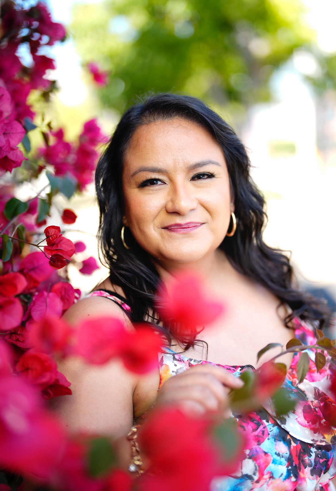 picture of owner in floral dress next to a red flower tree