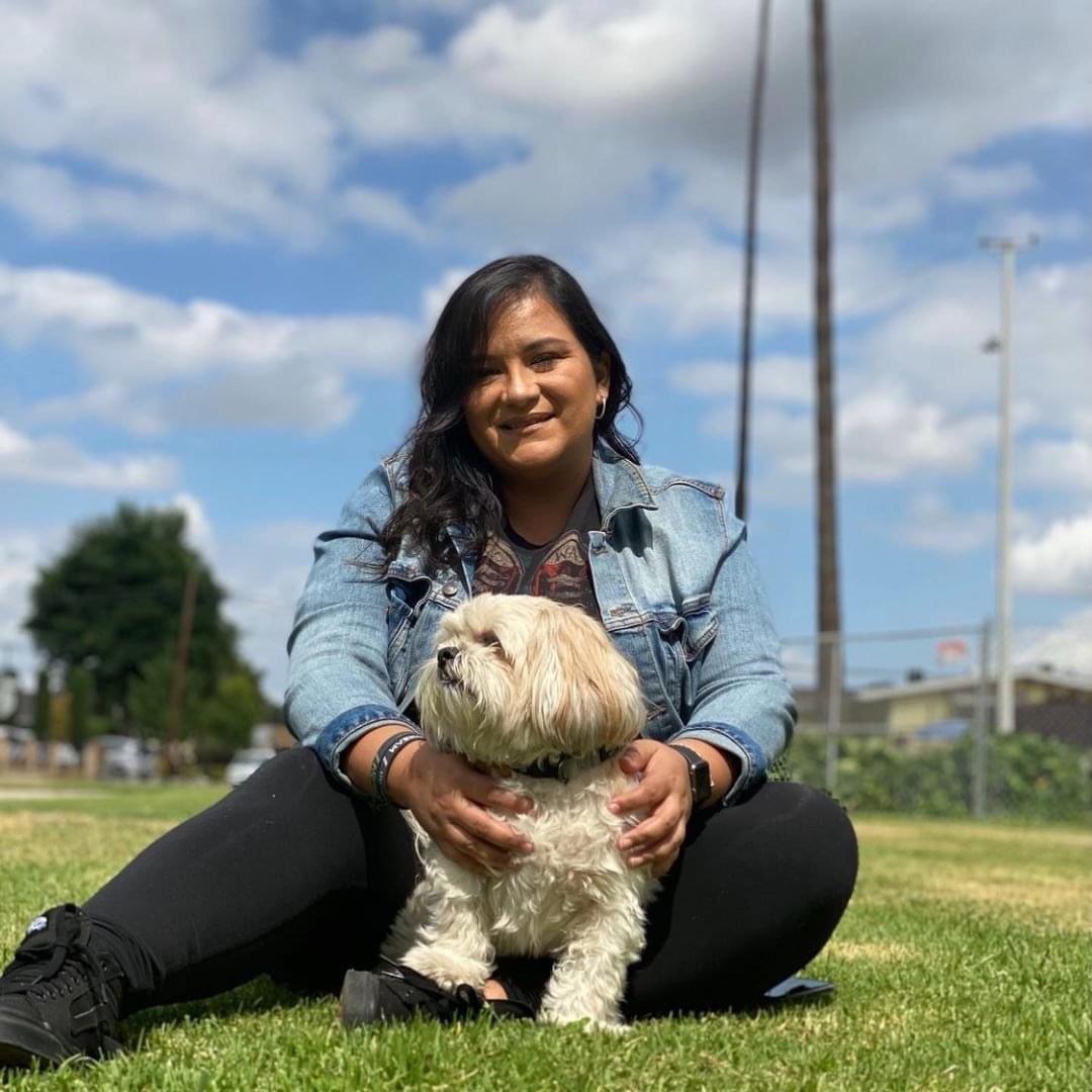 picture of owner sitting in the grass hold a white dog